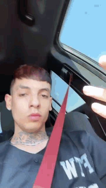 a young man is sitting in a car with a red seat belt around his neck .