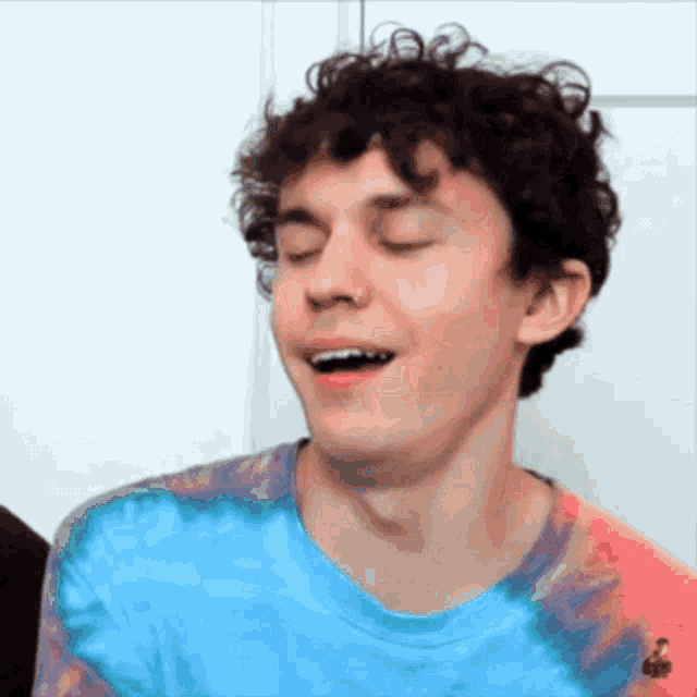 a young man with curly hair is wearing a blue and red tie dye shirt .