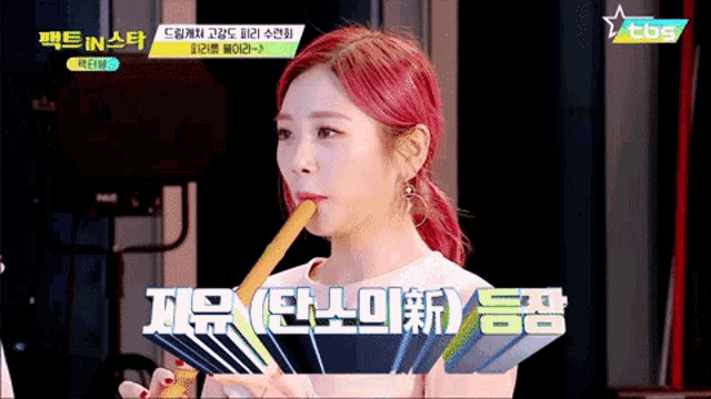 a woman with red hair is playing a flute with tbs on the bottom right