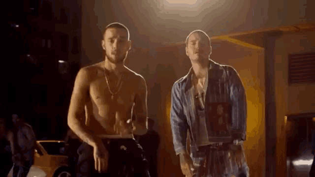 two men are standing next to each other in a dark room .