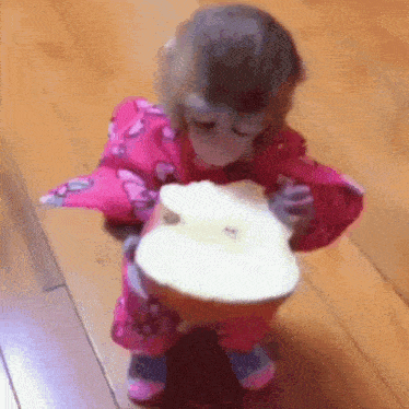 a baby monkey in a pink outfit is eating a piece of apple .