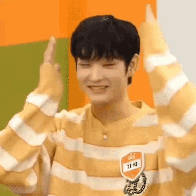 a young man wearing a yellow and white striped sweater is smiling and making a peace sign .