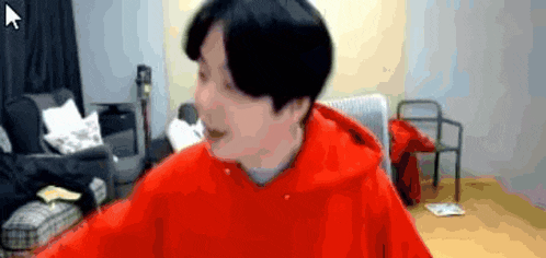 a man in a red hoodie is sitting in a living room with a chair .