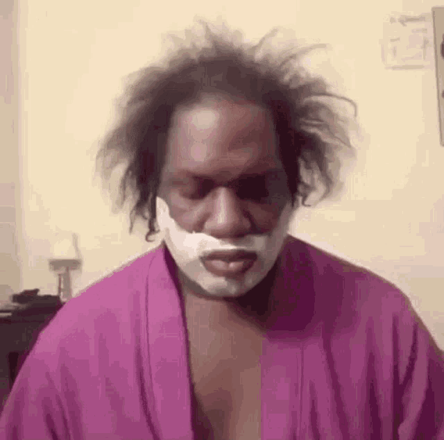 a man with a bandage on his face is wearing a purple robe and shaving his face .