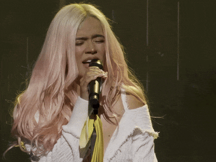 a woman with pink hair is smiling while singing into a microphone