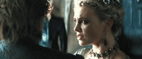 a man and a woman are looking at each other in a room . the woman is wearing a crown and earrings .