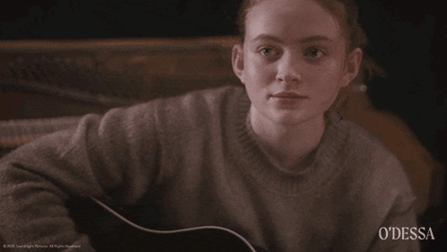 a girl sitting on a couch holding a guitar with odessa written on the bottom right