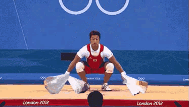 a man is squatting down on a wrestling mat at the london olympics