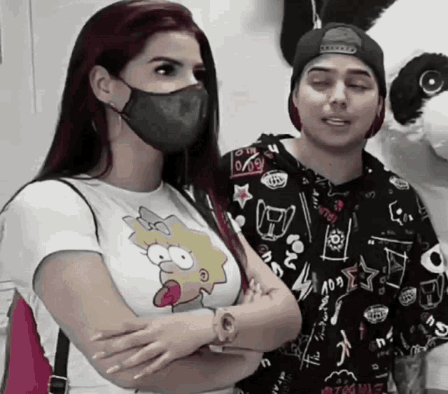 a woman wearing a mask stands next to a man wearing a shirt with a simpson on it