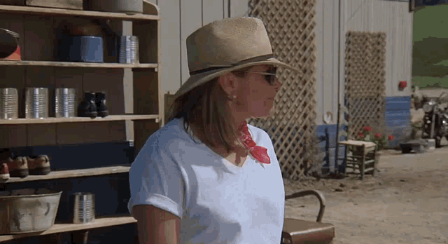 a woman wearing a hat and sunglasses stands in front of a shelf