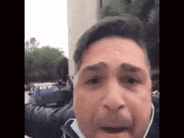 a man wearing a mask looks at the camera with a blue car in the background .