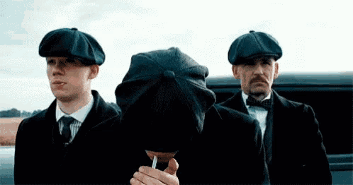 a man in a hat is smoking a cigarette while standing next to two other men .