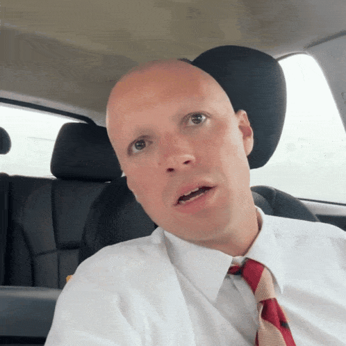 a bald man wearing a white shirt and red tie looks at the camera