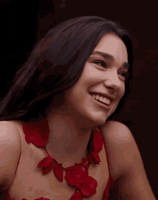 a woman in a red dress is smiling and wearing a red necklace with red flowers .