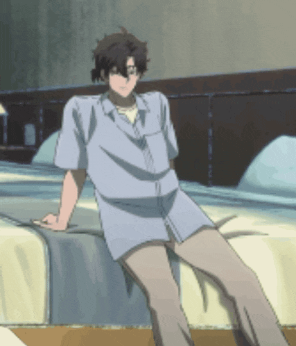 a man in a blue shirt sits on a bed with his legs crossed