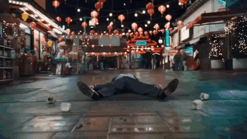 a person is laying on the ground in a street with lanterns hanging from the ceiling .