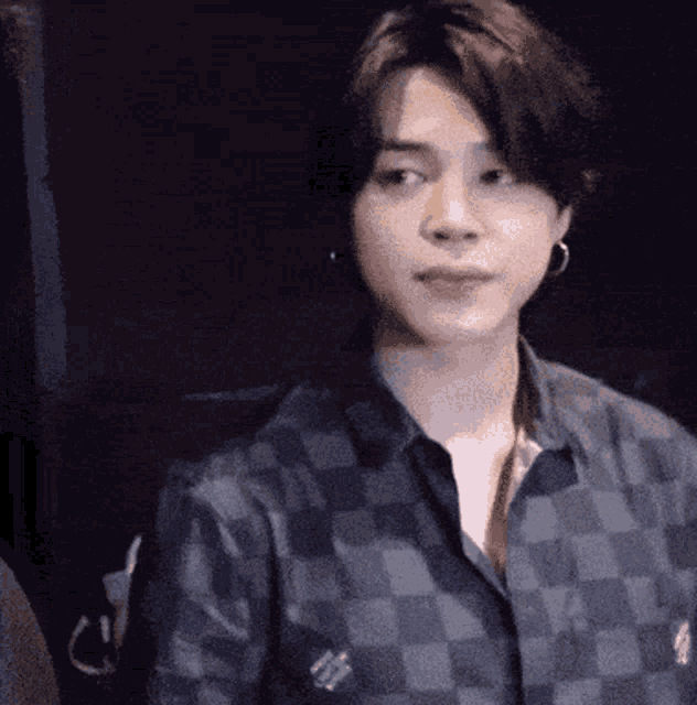 a young man wearing a plaid shirt and earrings is standing in a dark room .