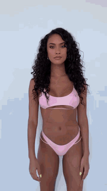 a woman in a pink bikini top and bottom stands in front of a white wall