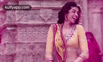 a woman in a yellow and pink dress is laughing while standing in front of a stone wall .