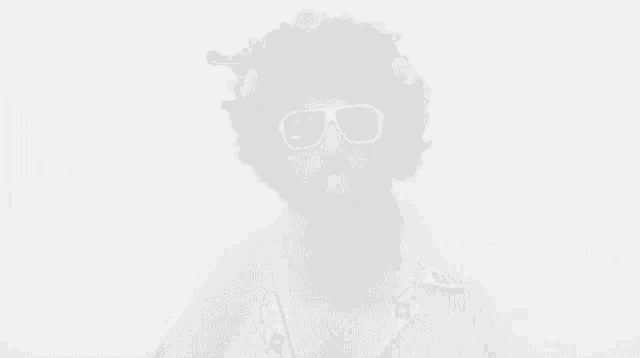 a man with a beard wearing an afro and sunglasses blowing a bubble