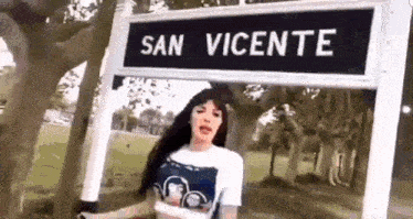 a woman is standing in front of a street sign that says san vicente .