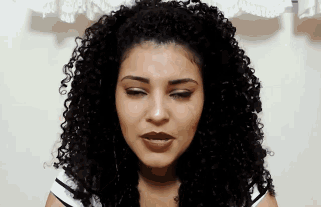 a woman with curly hair is making a face with her eyes closed