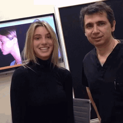 a man and a woman are posing for a picture in front of a television