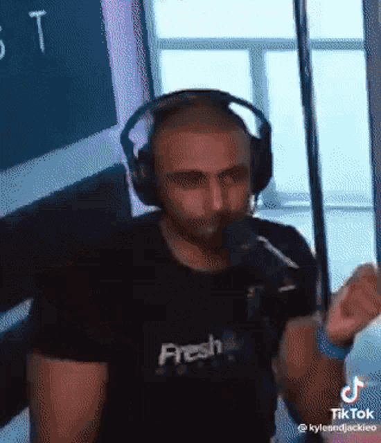 a man wearing headphones and a fresh shirt stands in front of a microphone