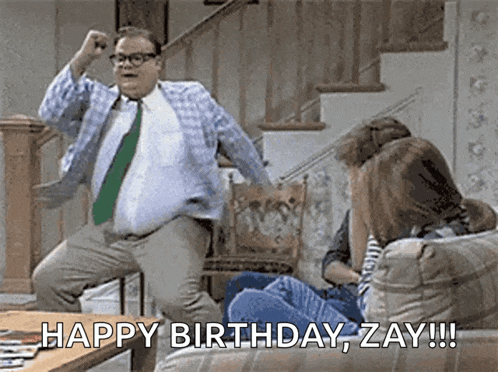 a man in a tie is jumping in the air while a woman sits on a couch and says happy birthday zay !!!