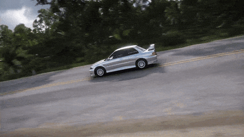 a silver car is driving down a road with trees on the side