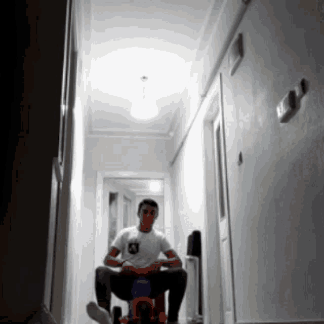 a man in a white shirt is sitting on a toy bike in a hallway