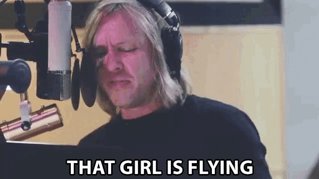 a man wearing headphones is singing into a microphone and saying that girl is flying