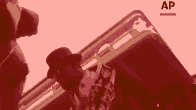 a man in a hat is standing next to a briefcase with the letters ap above him