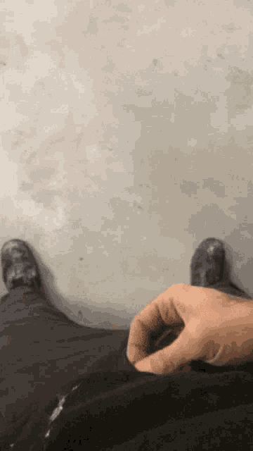 a person 's feet are visible on a concrete floor and a hand is visible in the foreground