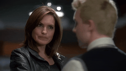 a woman in a black leather jacket looks at a man in a white shirt