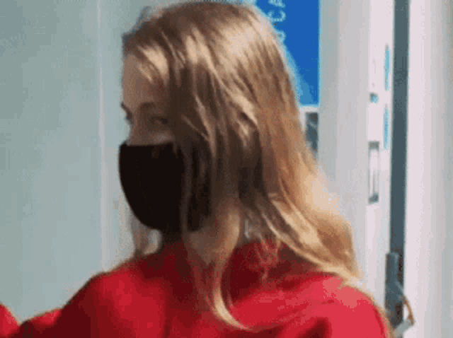 a woman wearing a red sweater and a black mask is standing in a hallway .