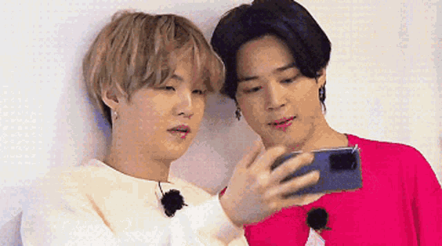 a couple of men are looking at a cell phone together .