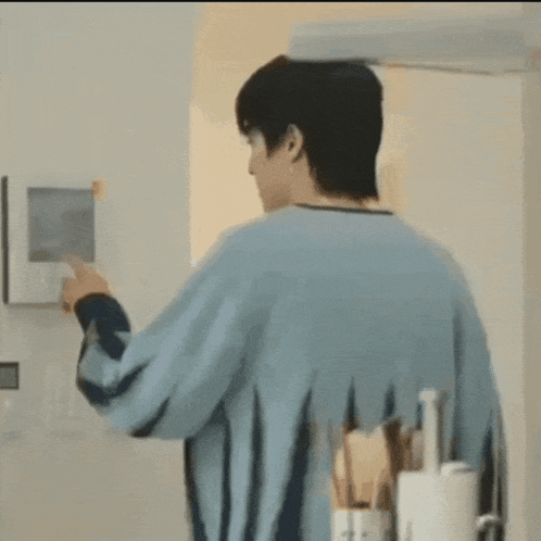 a man in a blue sweater is standing in front of a wall mounted monitor .