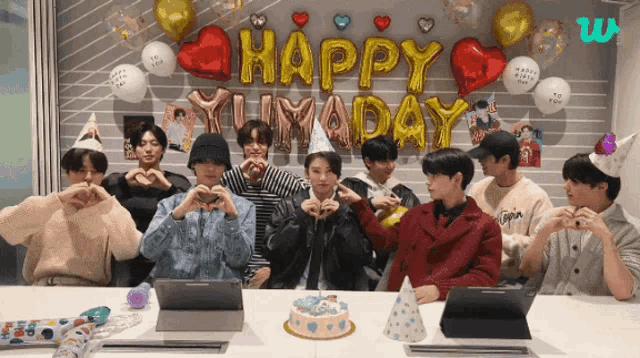 a group of young men are sitting at a table in front of balloons that say " happy birthday "
