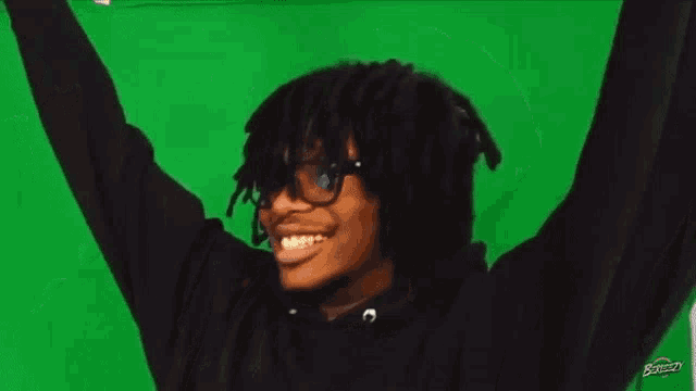 a man stands in front of a microphone with his arms in the air in front of a green screen that says boomcity
