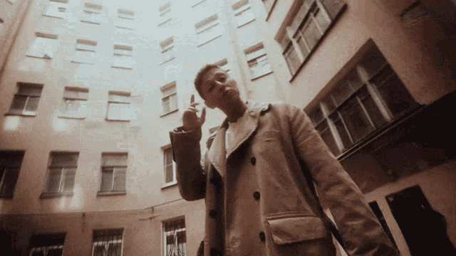 a man in a tan coat stands in front of a large building
