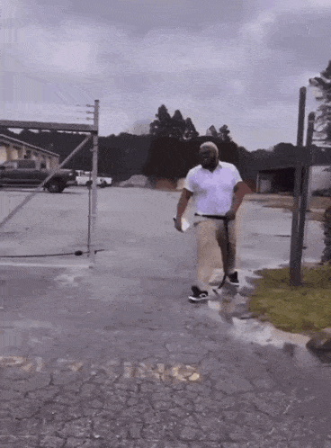 a man in a white shirt is walking in a parking lot with a fence in the background