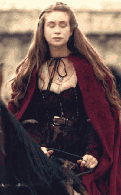 a woman wearing a red cape is riding a black horse