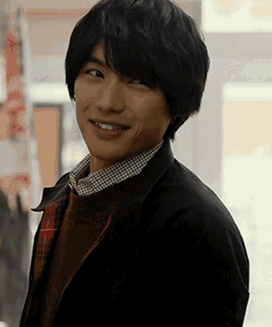 a young man wearing a plaid shirt and a black jacket is smiling