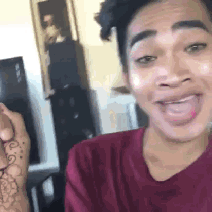 a young man in a red shirt is making a funny face while holding a tattoo on his arm .