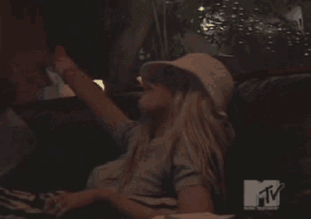 a woman wearing a hat is sitting in front of a tv screen that says mtv on it