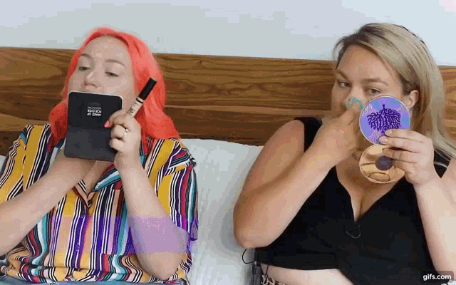 a woman with pink hair is holding a makeup brush while another woman holds a makeup sponge