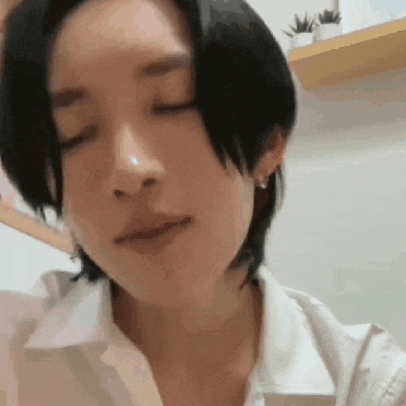 a close up of a woman 's face with her eyes closed . she is wearing a white shirt and earrings .