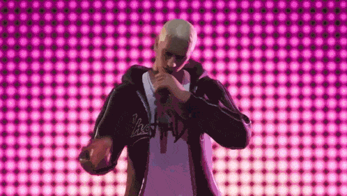 a man is singing into a microphone in front of a pink wall .