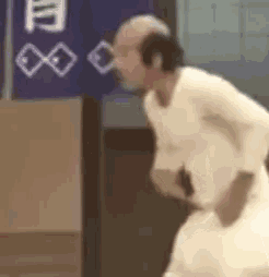 a bald man in a white shirt is standing in front of a sign .